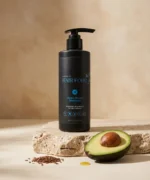 Hydra Boost Shampoo bottle sitting on a piece of natural stone. Surrounded by key ingredients like avocado